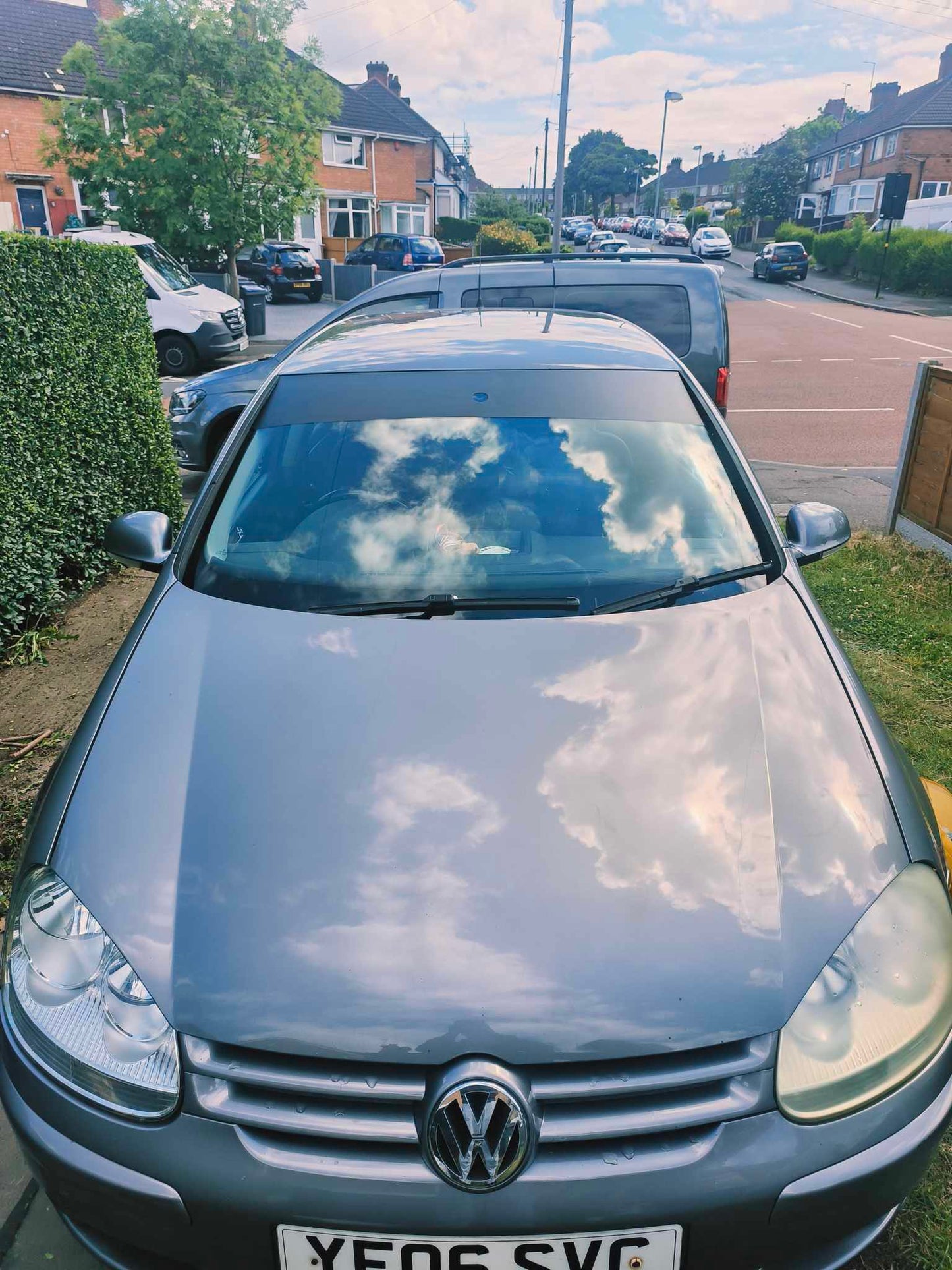 Volkswagen car parked on a residential street with houses and cars in the background.