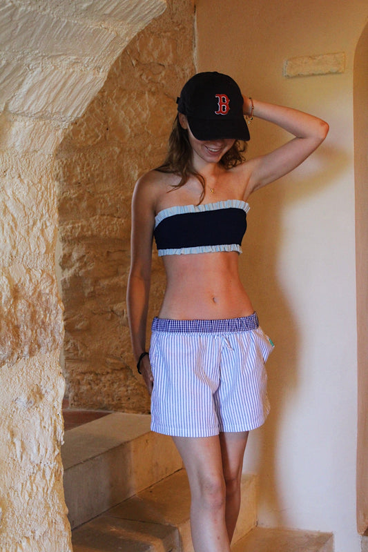 Woman wearing a black and white striped top and shorts with a baseball cap in a stone-walled room.