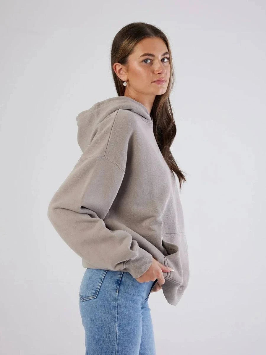 Woman wearing a gray hoodie and blue jeans against a white background
