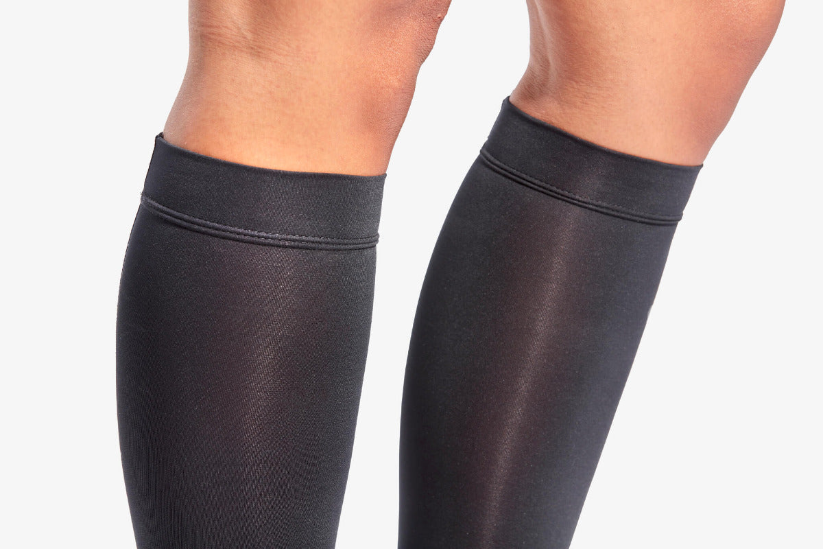 Black knee-high socks worn by a person on a light gray background