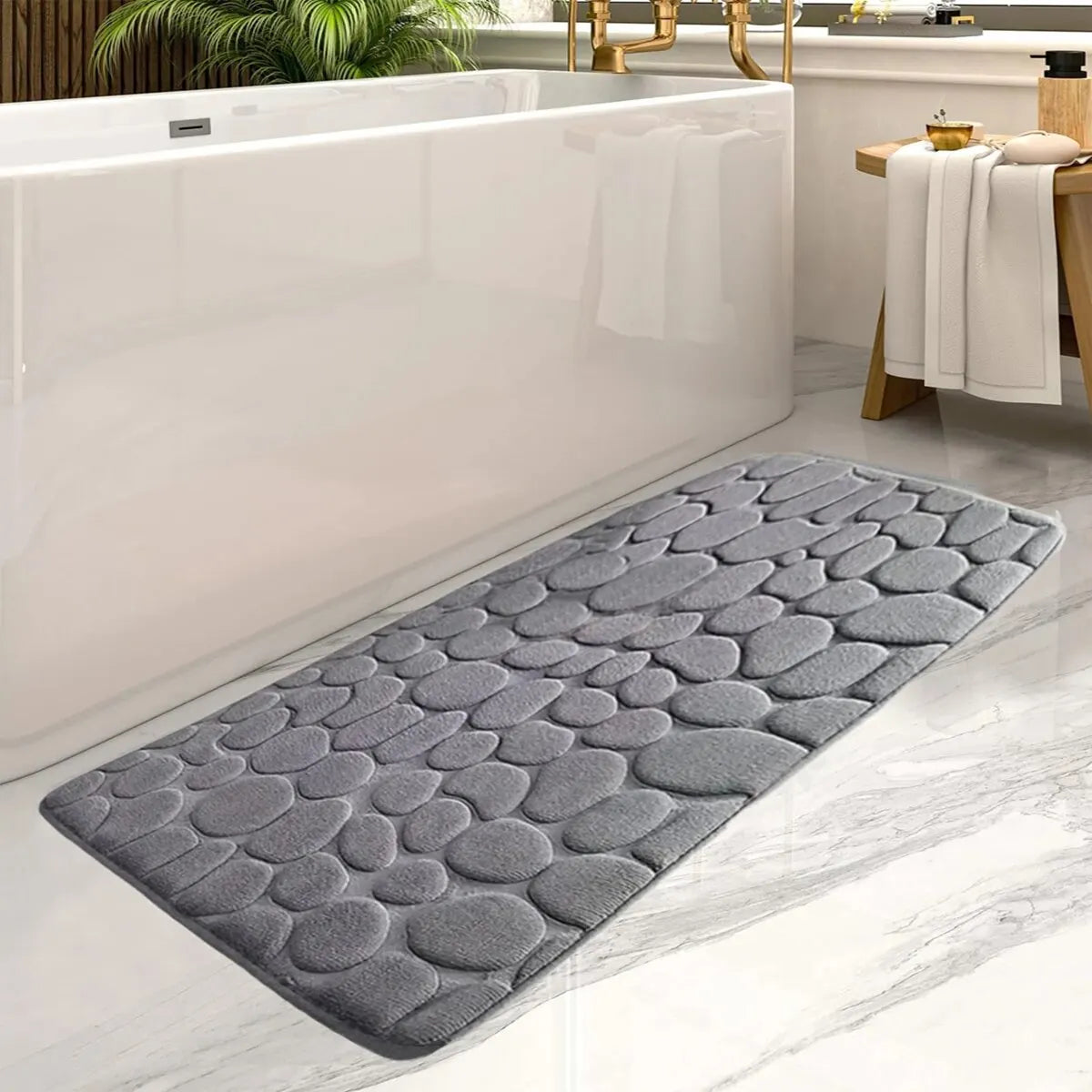 Gray textured bath mat in front of a white bathtub with a wooden stool and towels.