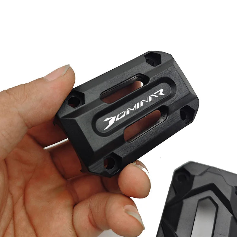 Black metal component with 'DOMINAR' branding held in a hand against a white background