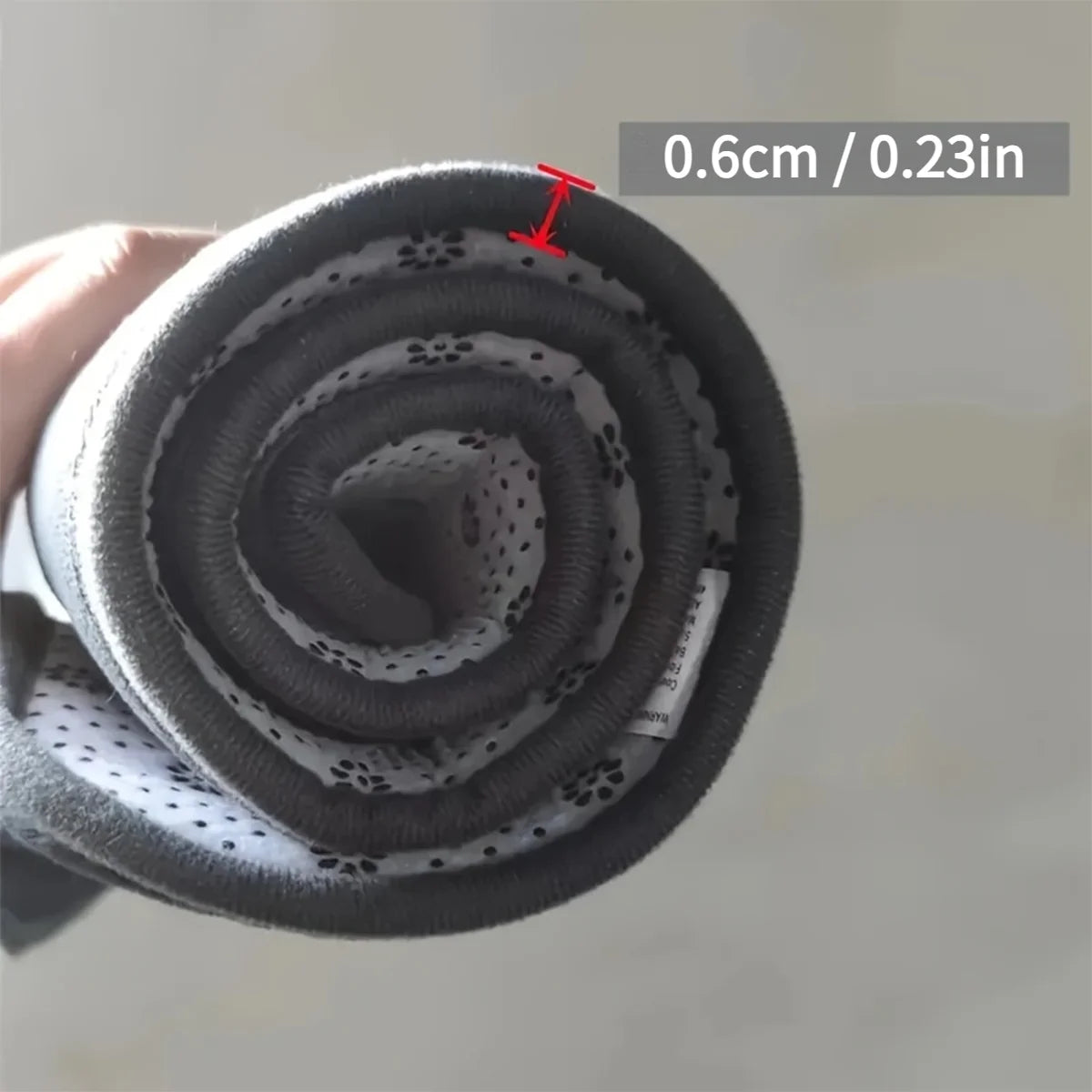 Coiled black flexible bathmat with measurement label on a neutral background