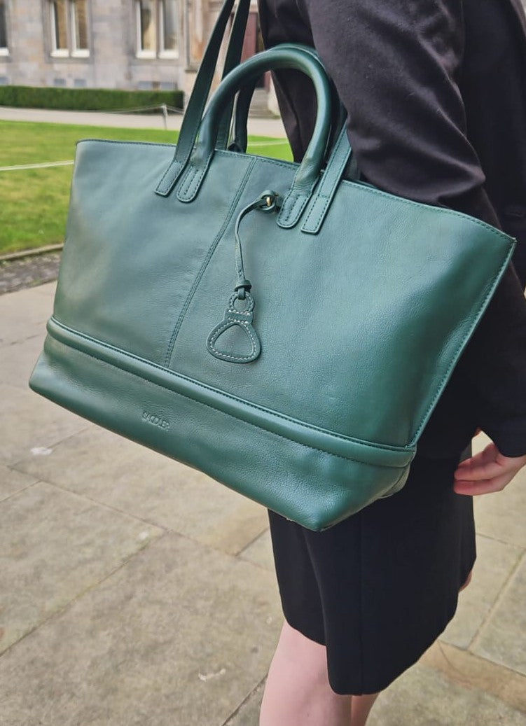 Green handbag held by a person outdoors on a stone path.