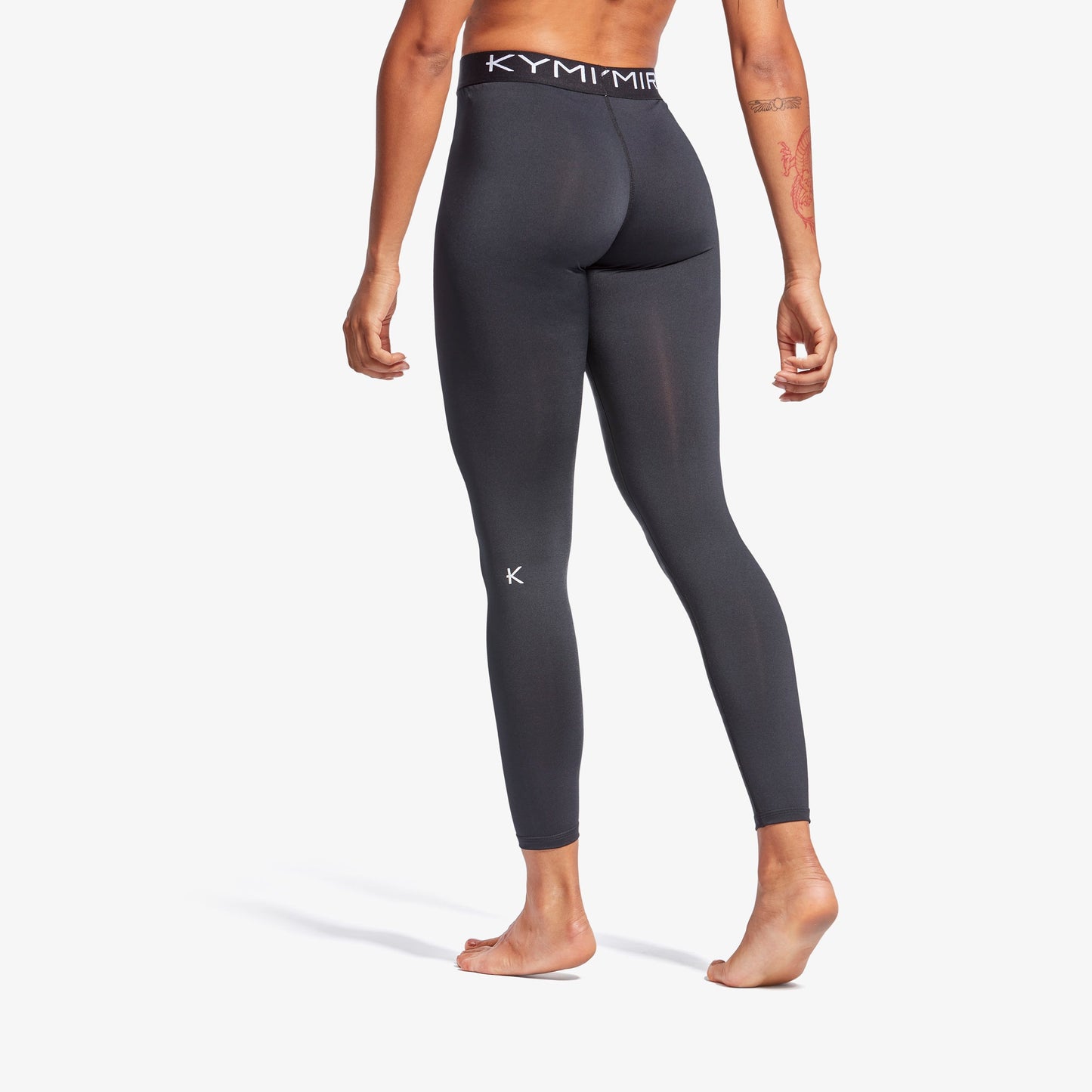 Person wearing dark gray leggings with a brand logo on a white background
