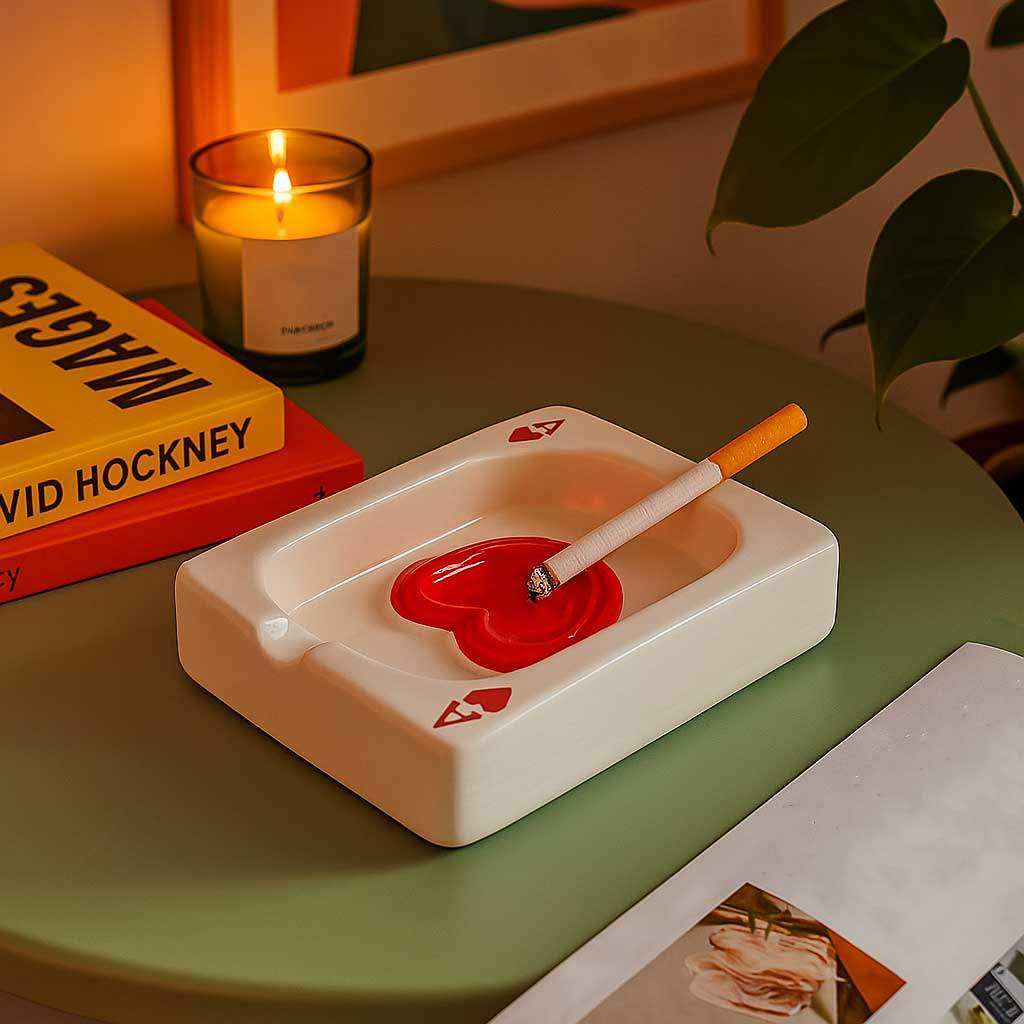 Ceramic ashtray with a red center on a table with a candle and books in the background