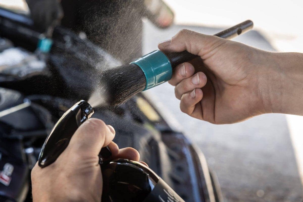 Person cleaning a motorcycle with a brush and spray bottle.