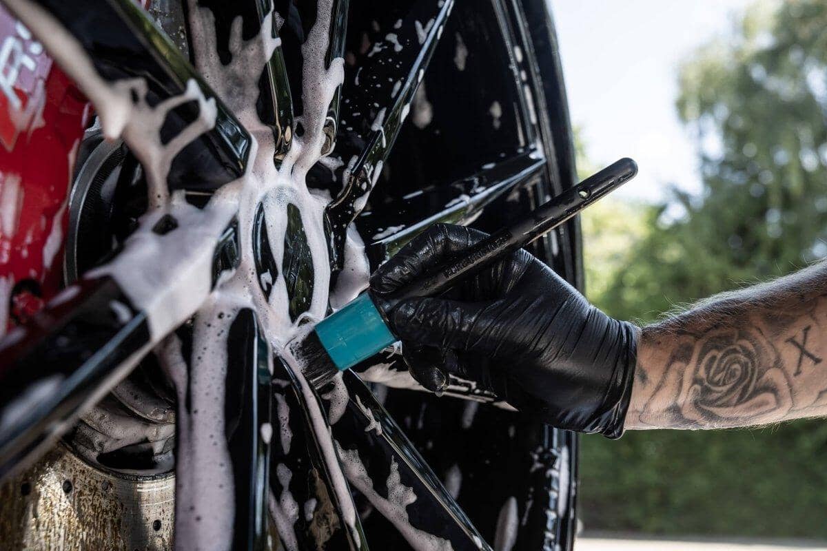 Person cleaning a car wheel with a brush and soap, outdoors.