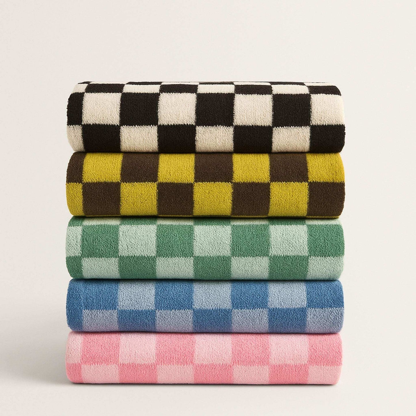 Stack of four checkered towels in black, yellow, green, and pink on a light gray background