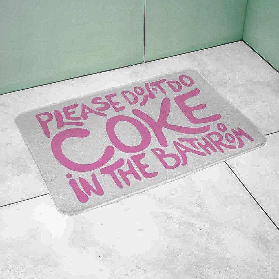 Gray bath mat with pink text on a tiled bathroom floor