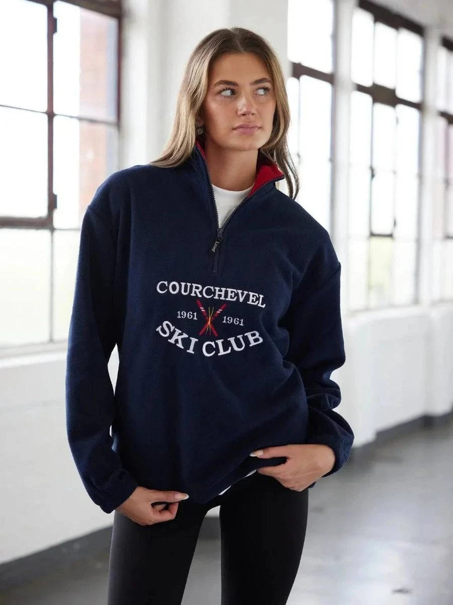 Woman wearing a navy blue sweatshirt with 'Courchevel Ski Club' text in an indoor setting.