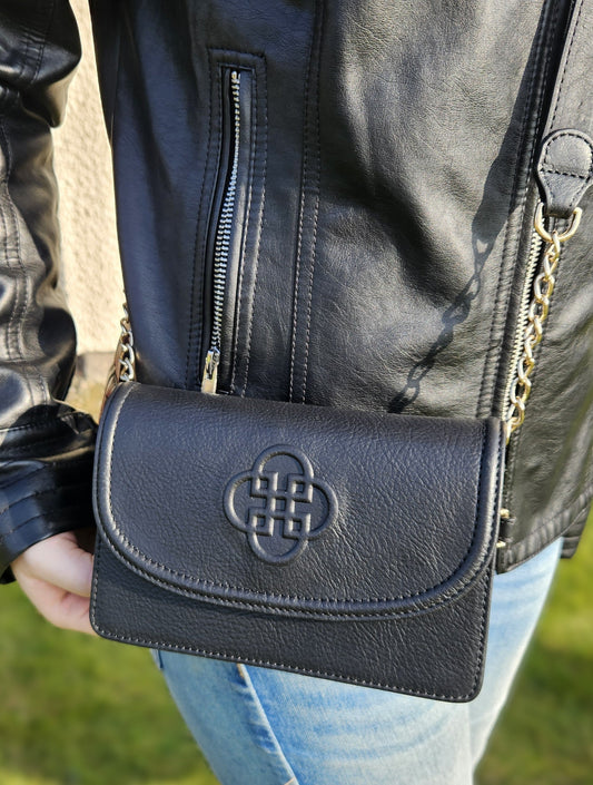 Black leather handbag with a distinctive logo held by a person wearing a black leather jacket.