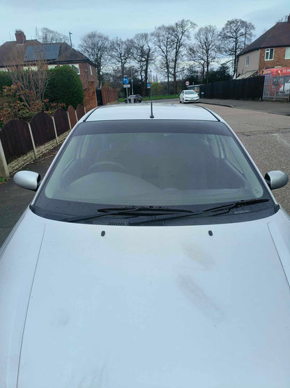 White car parked on a residential street with houses and trees in the background.