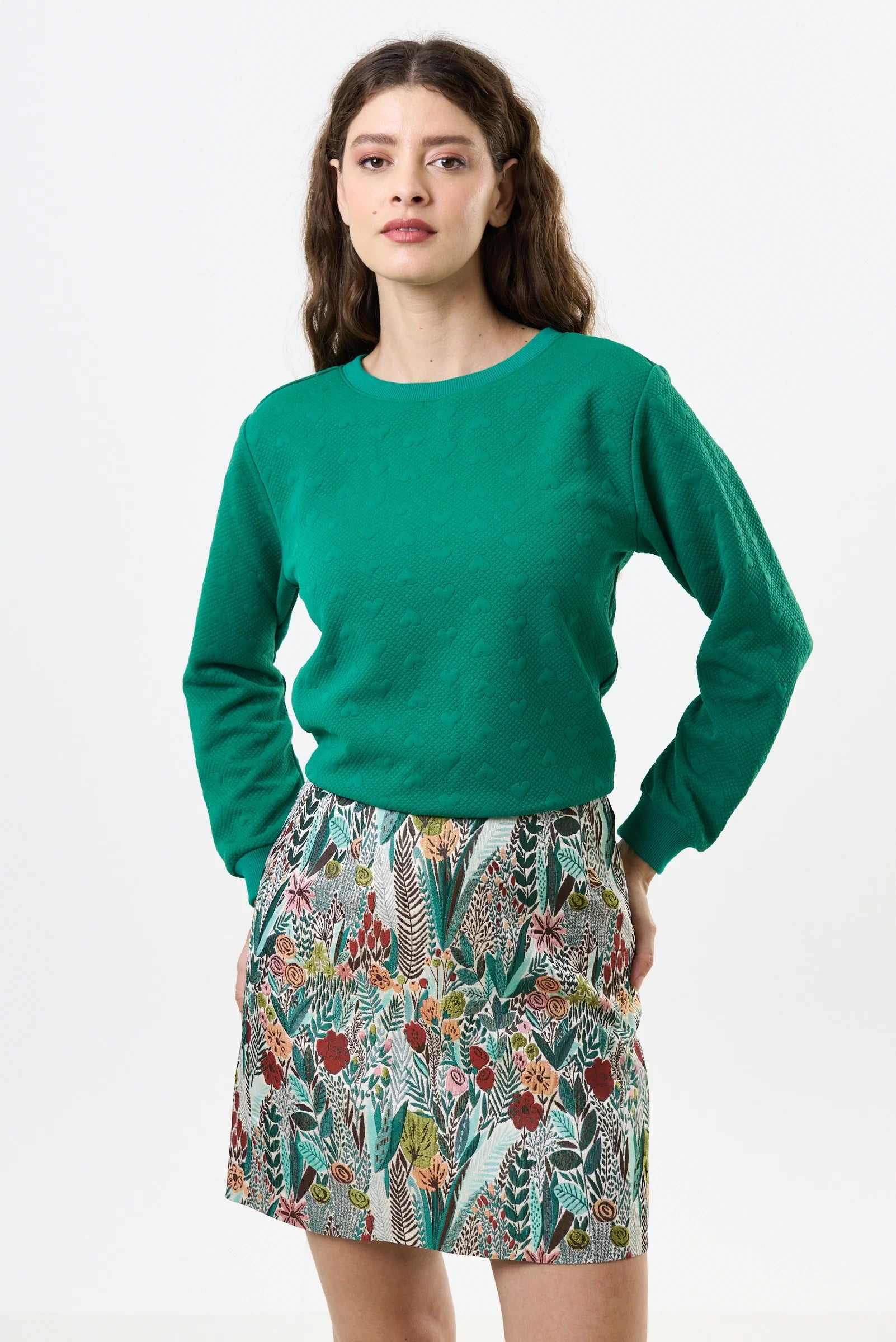 Woman wearing a green sweater and patterned skirt on a white background