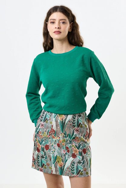 Woman wearing a green sweater and patterned skirt on a white background