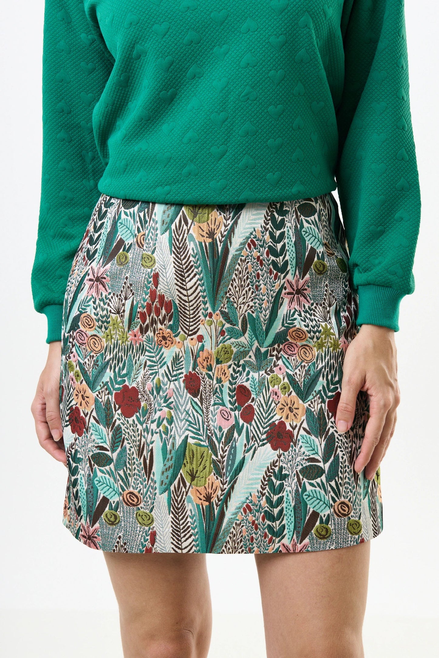 Person wearing a green sweater and floral skirt on a white background