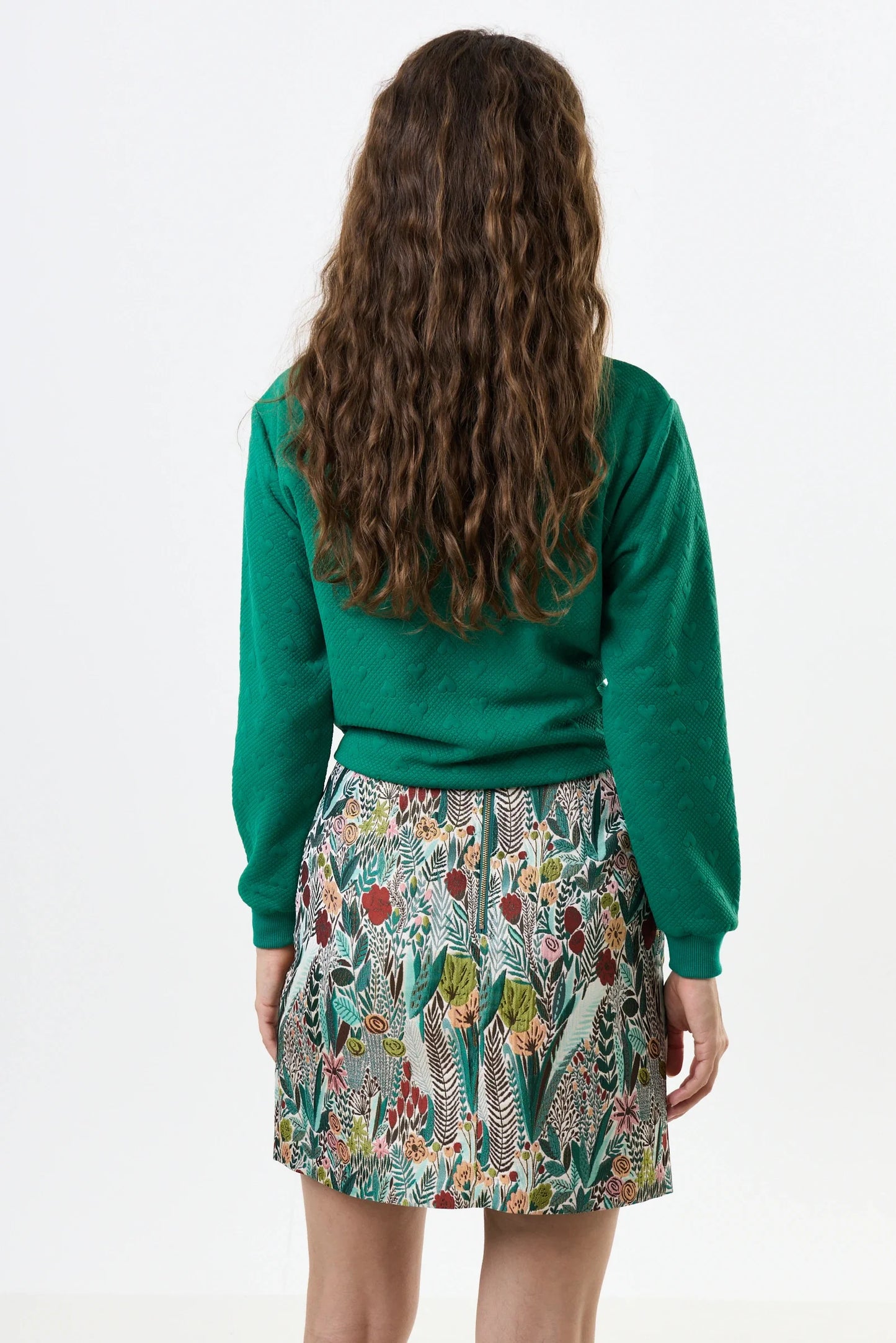Person wearing a green sweater and patterned skirt on a white background