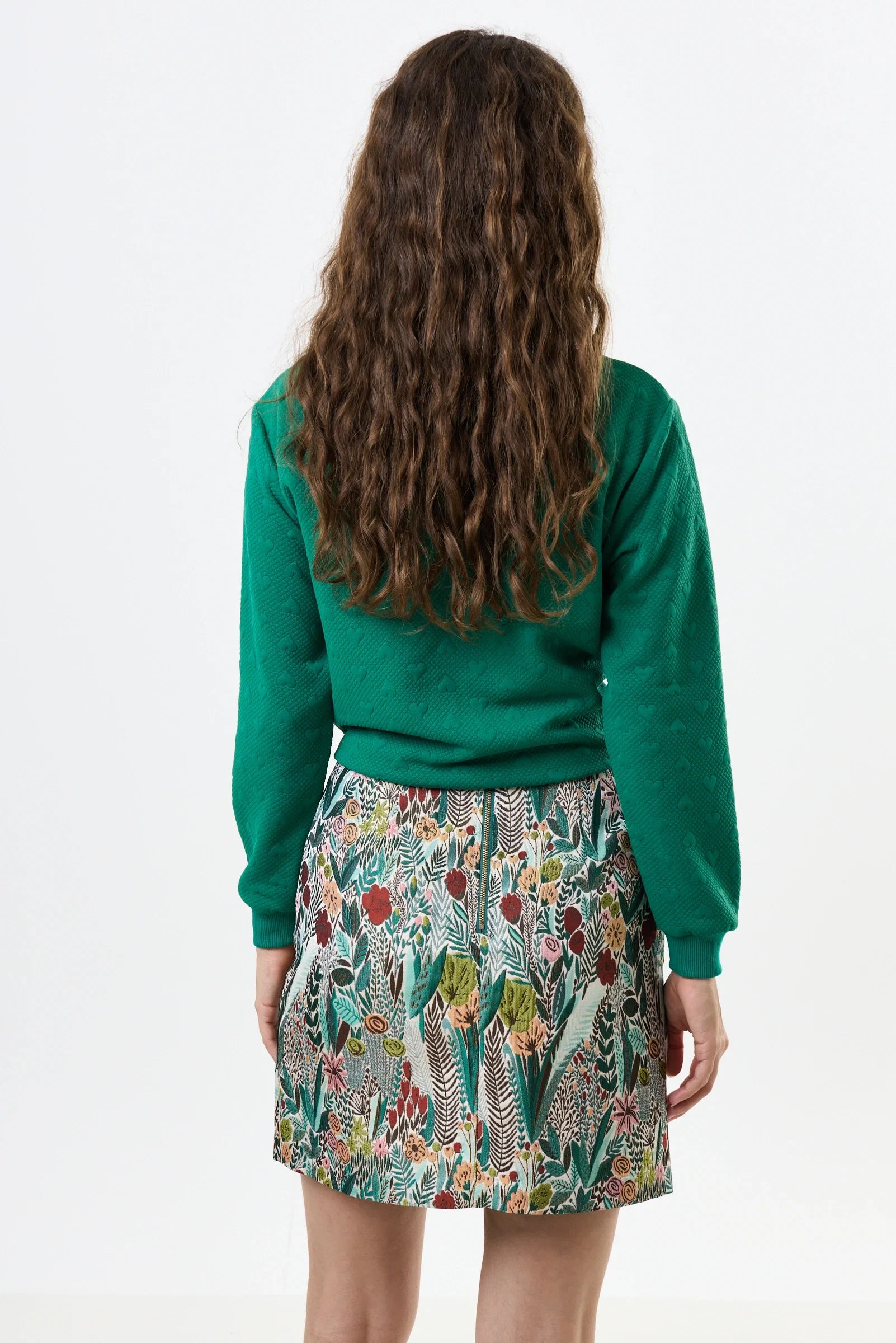 Person wearing a green sweater and patterned skirt on a white background