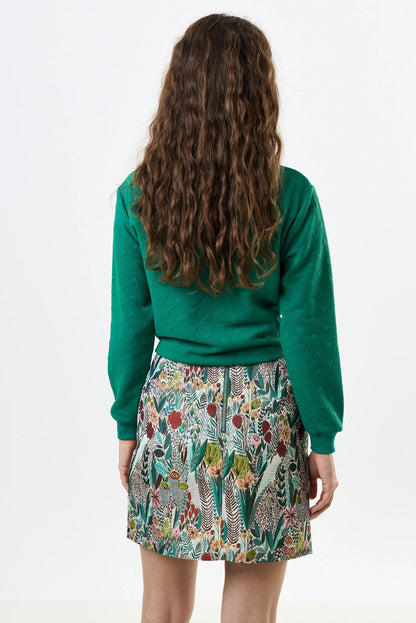 Person wearing a green sweater and patterned skirt on a white background