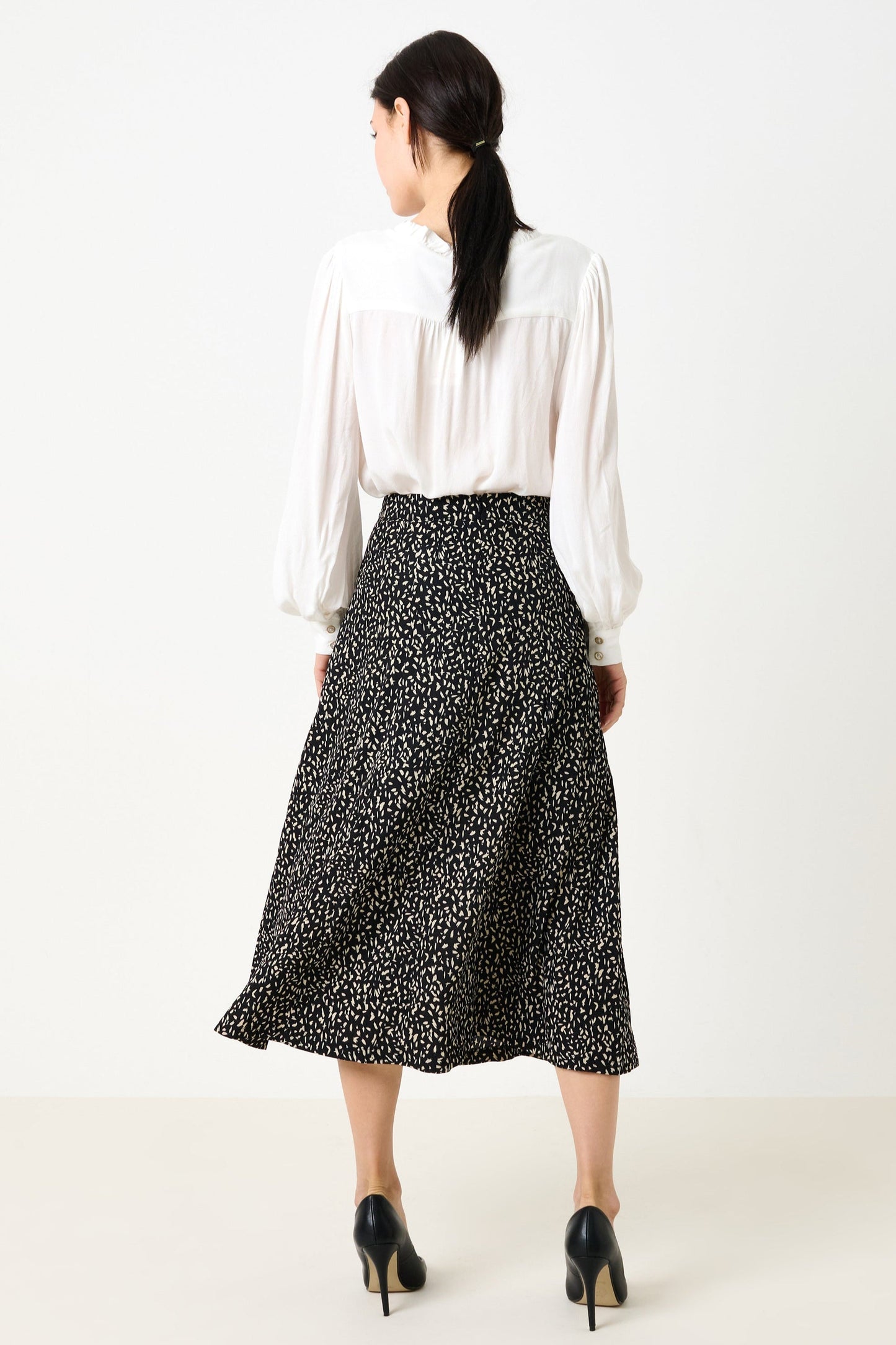 Woman wearing a white blouse and black patterned skirt on a white background