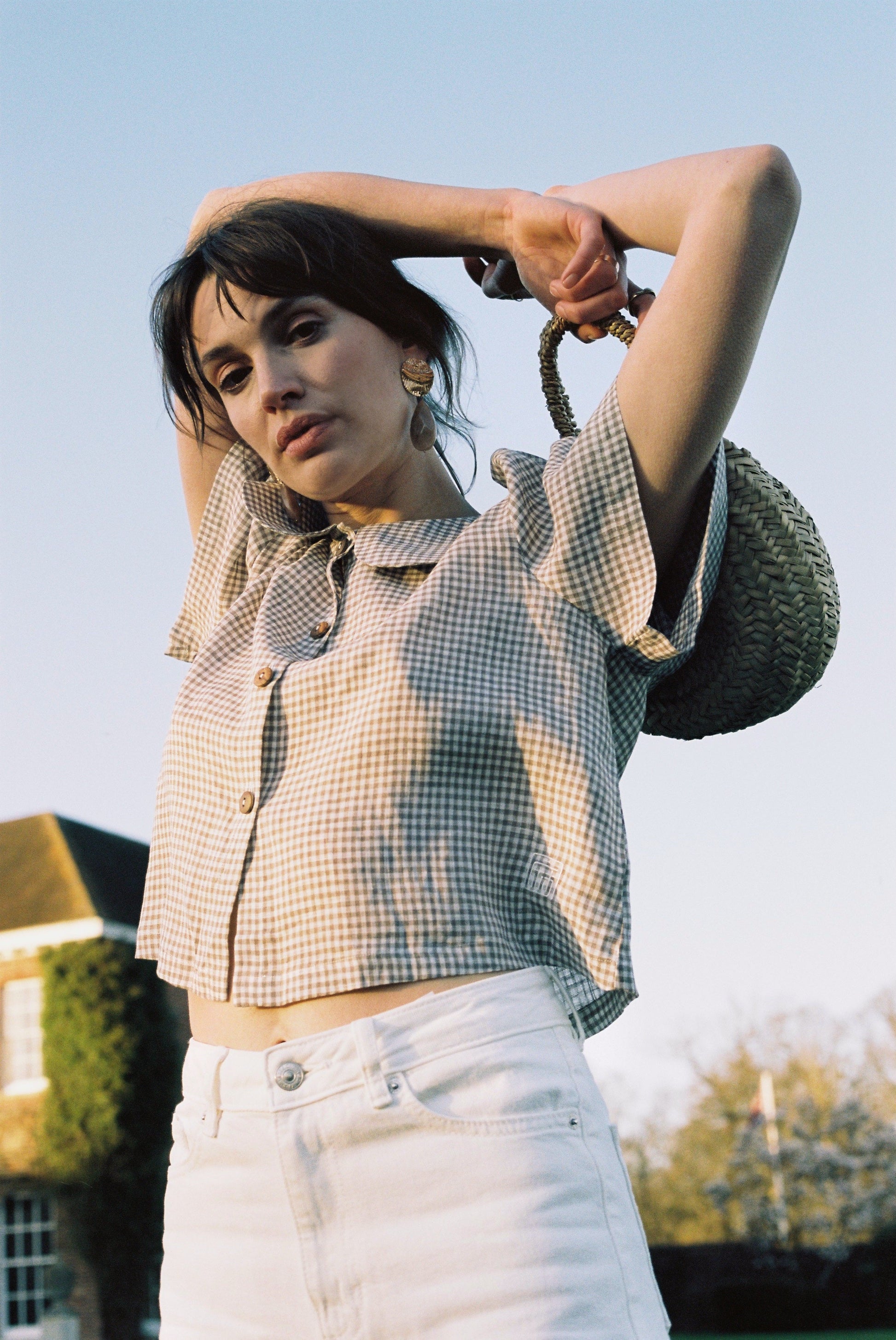 Woman wearing a checkered shirt and white pants with a straw hat, standing outdoors.