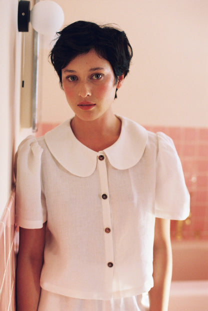 Woman wearing a white blouse with a large collar in a softly lit room.