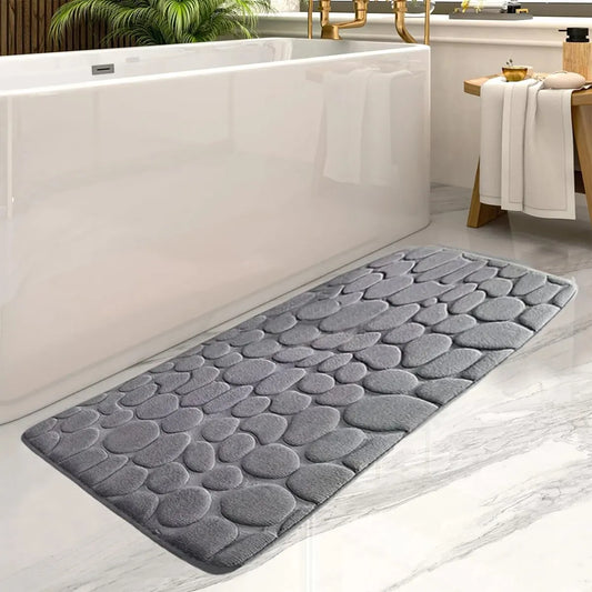 Gray textured bath mat in front of a white bathtub with a wooden stool and towels.