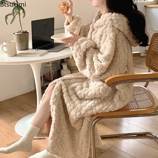 Person sitting on a chair wearing a fluffy beige blanket draped over their lap, with a laptop and cup on a table in the background.