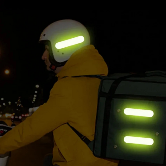 Person riding a motorcycle at night with glowing safety lights on helmet and backpack.