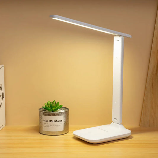 White LED desk lamp on a wooden surface with a small potted plant and book in the background.