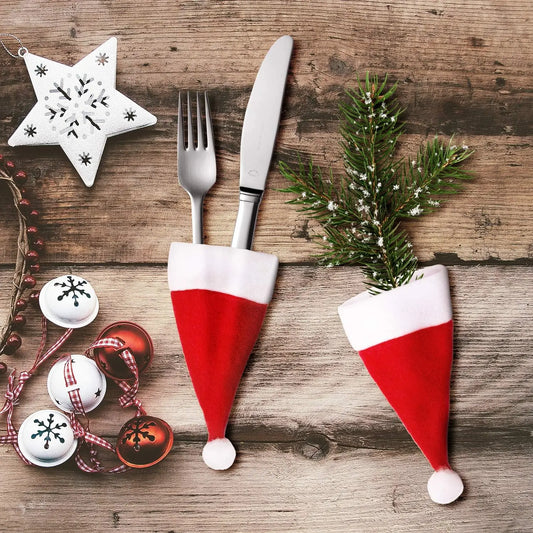 Santa hat cutlery holders on a wooden surface with Christmas decorations.
