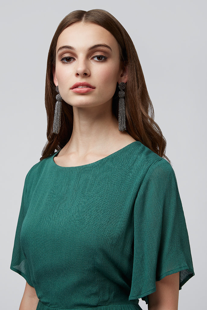 Woman wearing a green dress with tassel earrings on a gray background