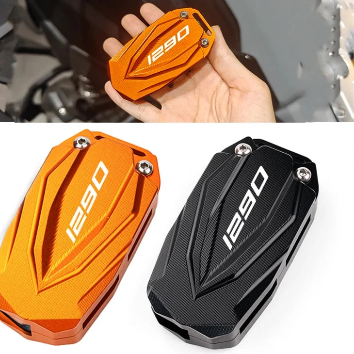 Orange and black motorcycle engine cover with '1290' branding, held by a hand against a blurred motorcycle background.