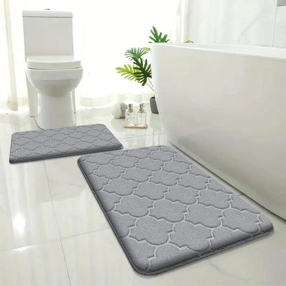 Gray bath mats on a bathroom floor with a toilet and bathtub in the background.
