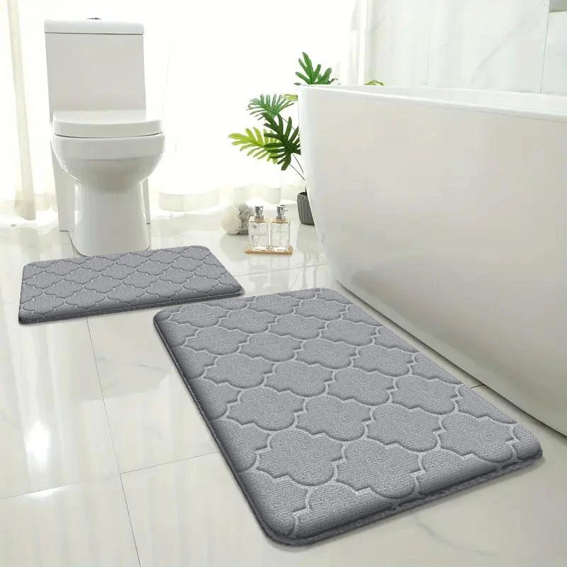 Gray bath mats on a bathroom floor with a toilet and bathtub in the background.