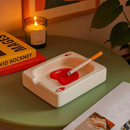 Ceramic ashtray with a red center on a table with a candle and books in the background