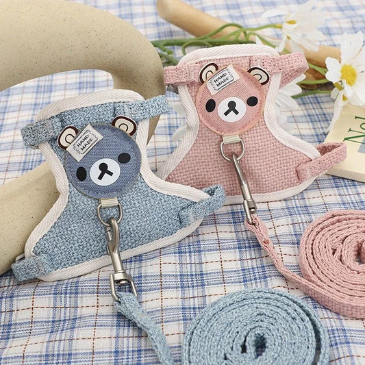 Two cute animal-themed dog harnesses, one blue and one pink, on a checkered fabric background.