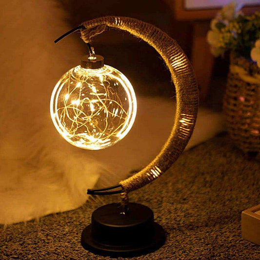 Decorative lamp with a glowing light bulb on a crescent moon-shaped stand.