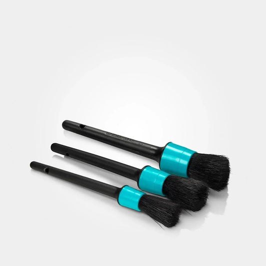 Three makeup brushes with black bristles and turquoise handles on a white background
