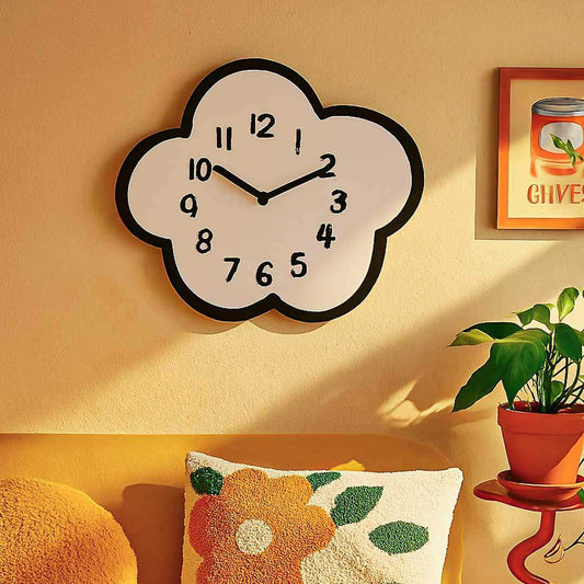 Cloud-shaped wall clock on a yellow wall with a plant and decorative pillow in the foreground.