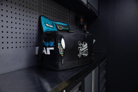 Black and teal tool bag with visible branding on a shelf against a dark wall.