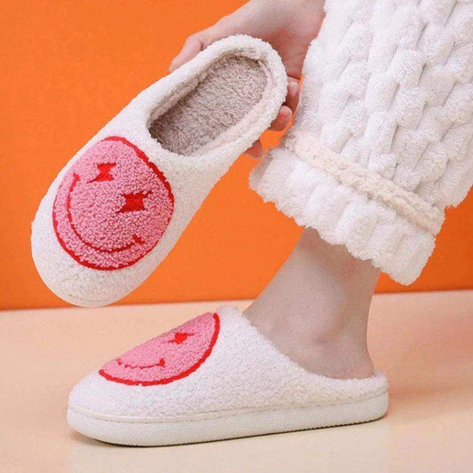 White slippers with pink smiley face design held by a person against an orange background