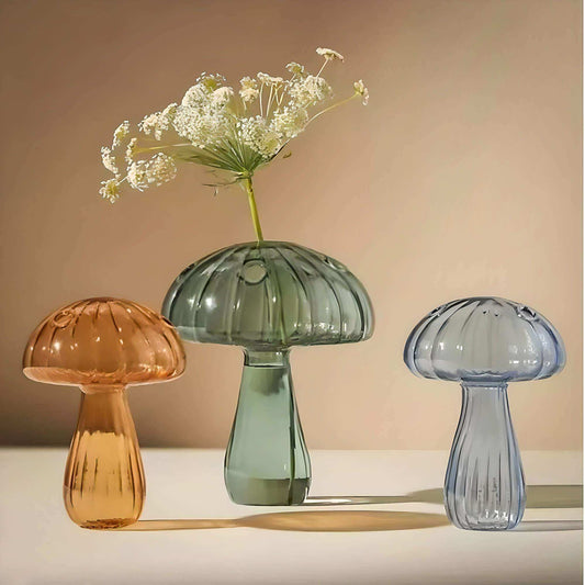 Three glass mushroom-shaped vases in orange, green, and blue on a neutral background