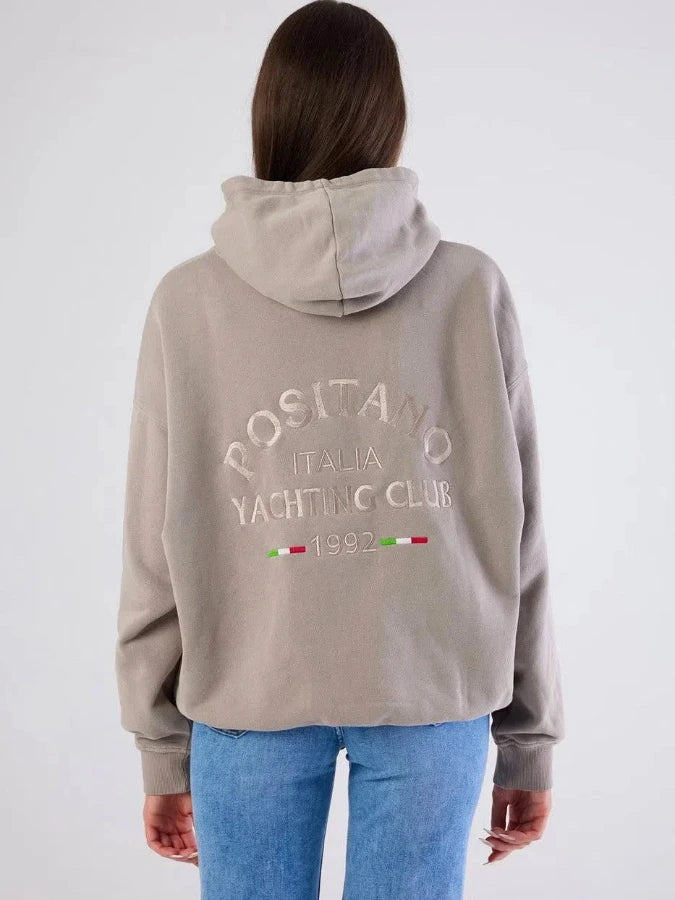 Person wearing a beige hoodie with text and logos on the back, standing against a white background