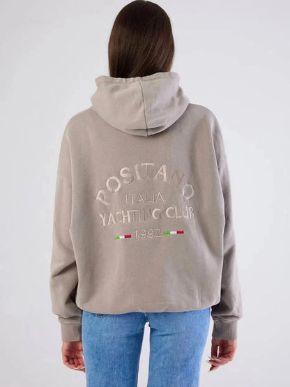 Person wearing a beige hoodie with text and logos on the back, standing against a white background