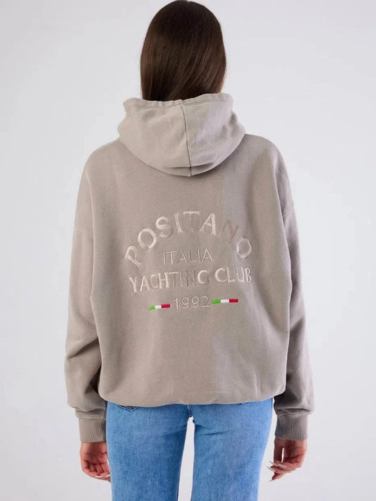 Person wearing a beige hoodie with text and logos on the back, standing against a white background