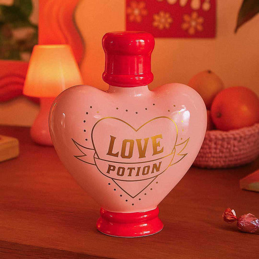Heart-shaped bottle labeled 'Love Potion' on a wooden surface with a warm background.