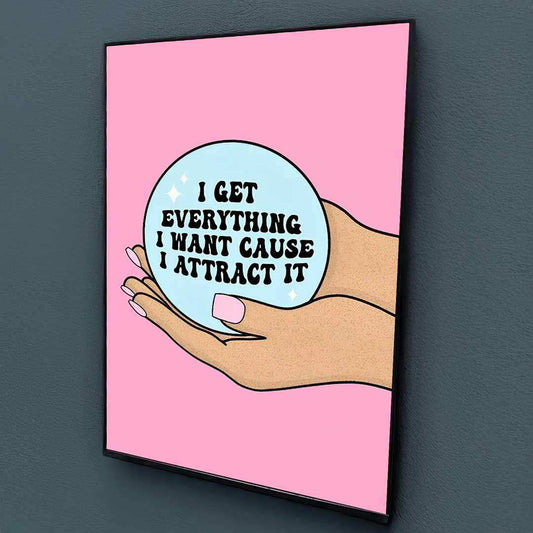 Framed artwork with a hand holding a bubble saying 'I get everything I want cause I attract it' on a pink background.