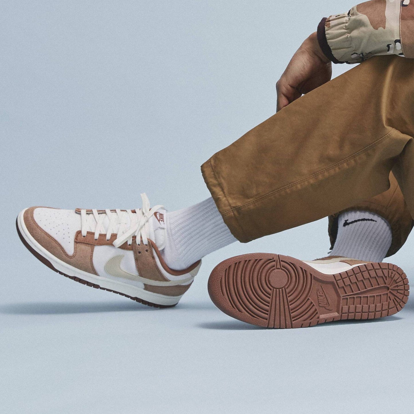 Brown and white sneakers worn with brown pants on a light blue background