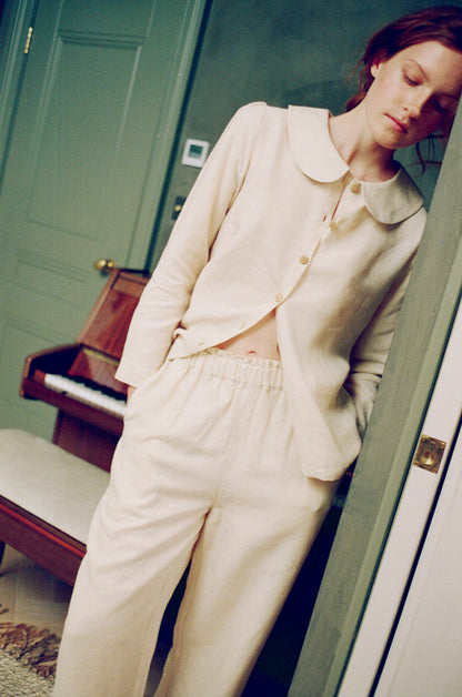 Woman in a cream-colored outfit standing in a room with a piano.